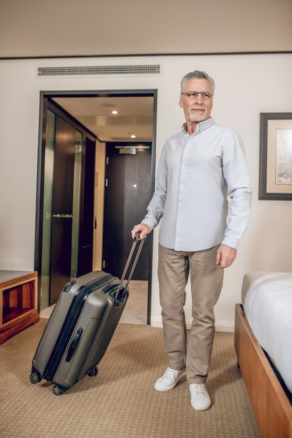 Reis. Grijsharige zelfverzekerde man met een koffer in een hotelkamer