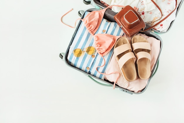 Reis handbagage met badpak bikini, slippers, zonnebril, jurk, retro camera op wit.