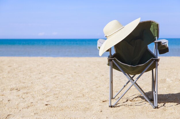 Reis naar de zee. campingstoel en hoed op het strand