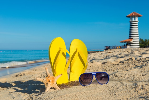 Reis naar de zee. Zonnige positieve strandvakantie. Gele sandalen, zonnebril, zeester en vuurtoren