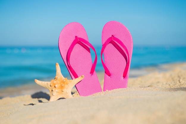 Reis over zee. Strand vakantie. Roze slippers en zeesterren aan zandige kust.