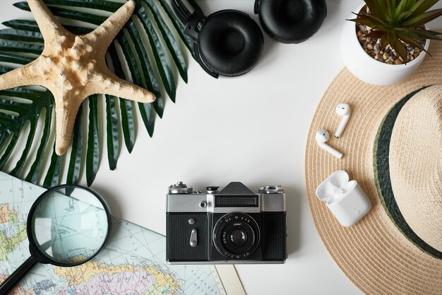Reis plat. Camera, koptelefoon, vergrootglas, tropische bladeren, strooien hoed op witte achtergrond