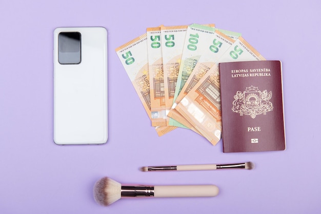 Reis plat met witte smartphone 50 euro bankbiljetten paspoort en make-upborstels op pastelachtergrond