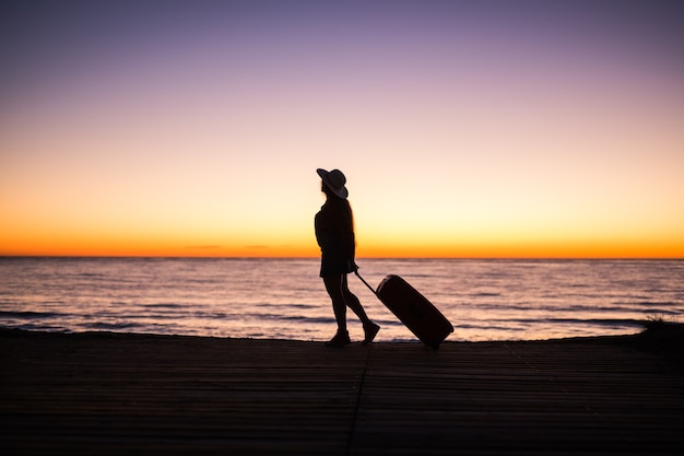 Reis-, strand- en vakantieconcept - Vrouwelijk silhouet wandelen langs de oceaankust koffer trekken.