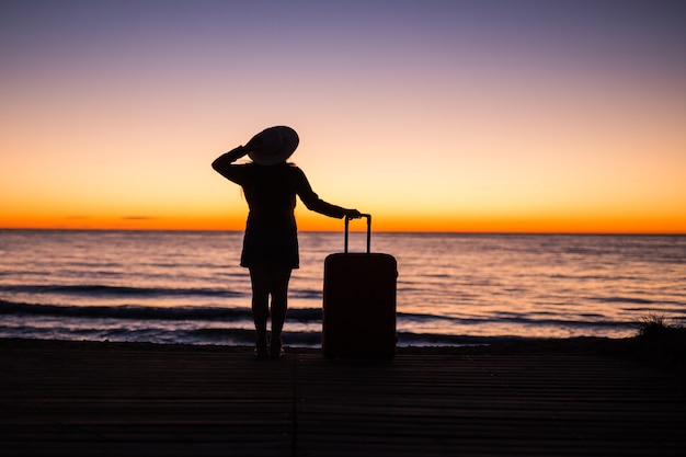 Reis-, vakantie- en zomervakantie concept - silhouet van jonge vrouw in zomerjurk en hoed op zoek naar een zee.