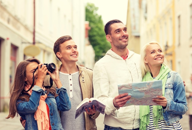 reis-, vakantie-, technologie- en vriendschapsconcept - groep lachende vrienden met stadsgids, fotocamera en kaart die de stad verkent