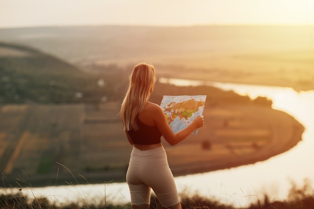 Reis vrouw leeskaart bij geweldige zonsondergang, geniet van het natuurlandschap. Ze houdt een toeristische kaart vast en plant een route in de bergen