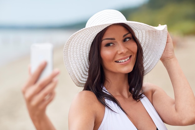 reis, zomer, technologie en mensenconcept - sexy jonge vrouw die selfie met smartphone op strand neemt