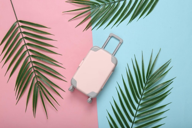 Foto reisbagage en palmgroene bladeren op roze blauwe achtergrond reisconcept tropische samenstelling bovenaanzicht plat leggen