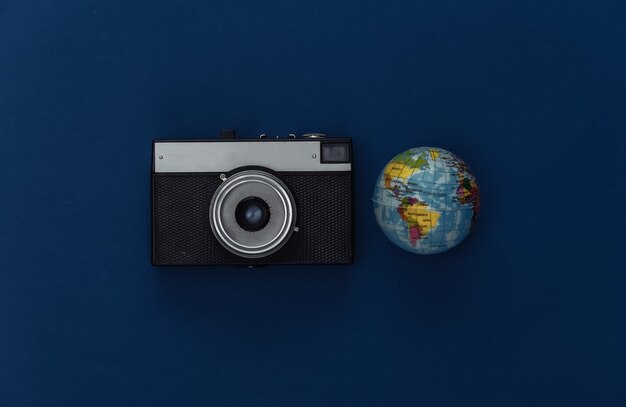 Reisconcept. Camera en globe op klassieke blauwe achtergrond. Kleur 2020. Bovenaanzicht.