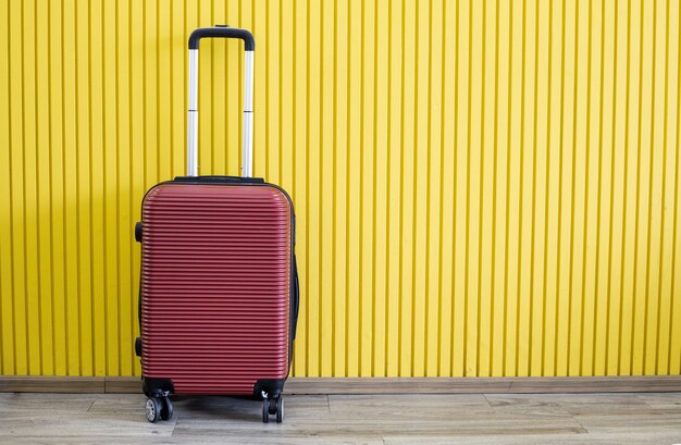Reisconcept, grote rode koffer op een houten vloer en hebben een gele achtergrond met kopieerruimte.