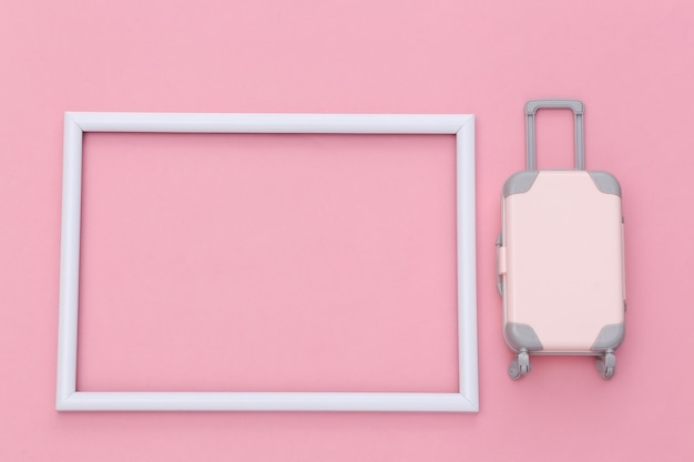 Reisconcept. Mini plastic reiskoffer op roze pastelachtergrond met wit frame voor uw tekst. Minimale stijl. Ruimte kopiëren. Bovenaanzicht, plat gelegd