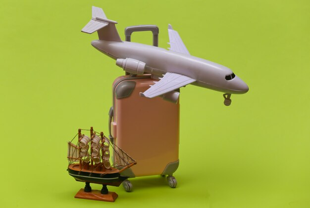 Reisconcept. mini plastic reiskoffer, schip en vliegtuig op groene achtergrond. minimale stijl