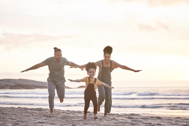 Reisvrijheid en een gezin op het strand tijdens zonsondergang om te vliegen, spelen en verbinden aan de oceaan Glimlachvakantie en een interraciaal kind, moeder en vader aan zee voor een vakantie of zomer