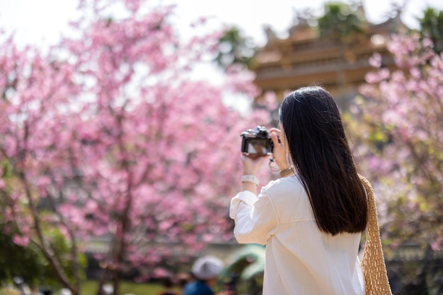 Reisvrouw gebruikt digitale camera om foto's te maken op de sakura boom