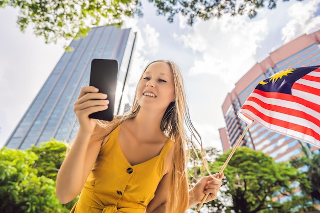 Reizen en technologie Jonge vrouwelijke toerist met de vlag van Maleisië kijkt naar een stadsplattegrond in een smartphone voor navigatie
