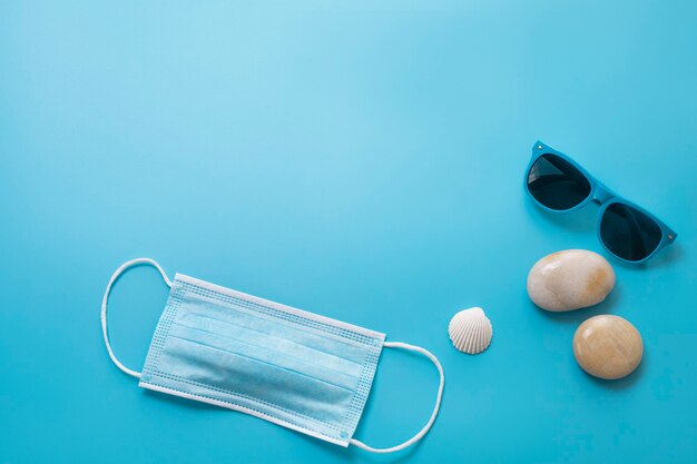 Reizen in de tijd van COVID-19. Medisch masker, zonnebril, zeeschelp op de blauwe achtergrond. Vrije ruimte voor tekst. Vakantie, vakantie in coronatijden. Kleurrijk ontwerp.