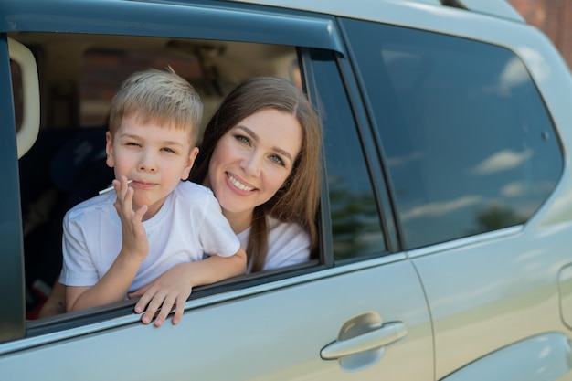 Reizen met de auto met het hele gezin Gelukkige blanke vrouw met lachende zoon die op de achterbank van een SUV zit en uit een raam kijkt Autorit op zomervakantie
