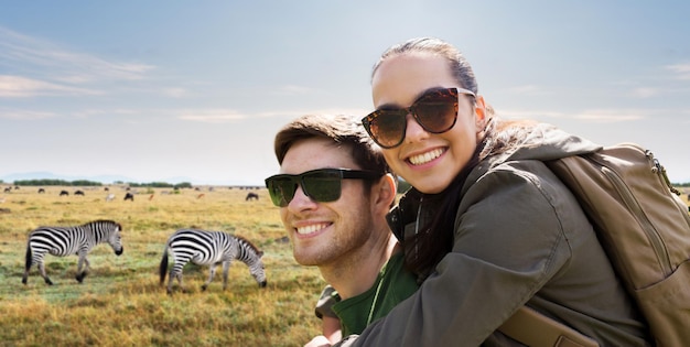 Foto reizen, toerisme en mensenconcept - gelukkig stel met rugzakken met plezier over de achtergrond van de afrikaanse savanne en zebra's