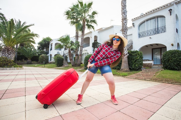 Reizen, toerisme en vakantie concept. grappige jonge vrouw die haar zware koffer trekt.