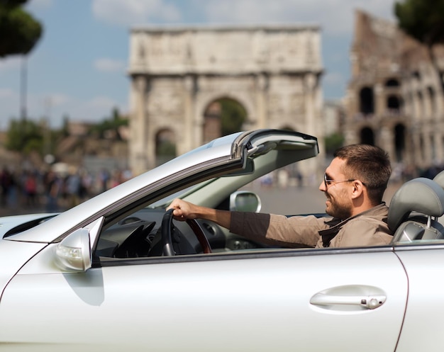 reizen, toerisme, road trip, transport en mensen concept - gelukkige man cabriolet auto rijden over triomfboog op de achtergrond van de stad rome