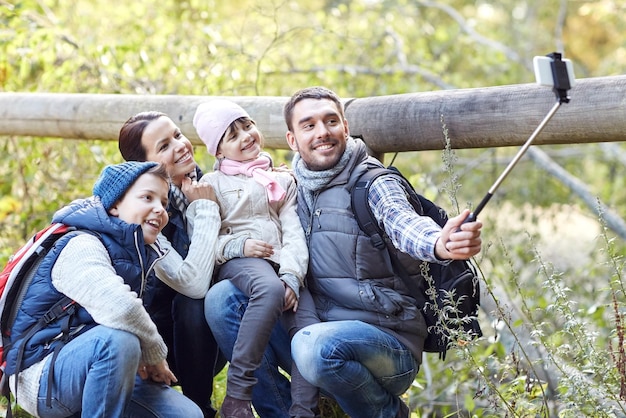 Foto reizen, toerisme, wandeling, technologie en mensenconcept - gelukkig gezin met rugzakken die foto's maken met smartphone en selfiestick in het bos