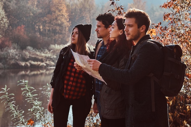 Reizen, wandelen, avontuur concept. groep jonge vrienden wandelen in het kleurrijke herfstbos, kijken naar kaart en plannen van een wandeling.