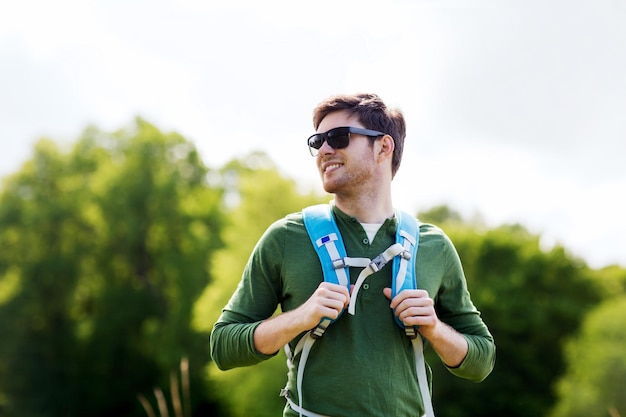 reizen, wandelen, backpacken, toerisme en mensen concept - gelukkige jonge man in zonnebril met rugzak buiten wandelen