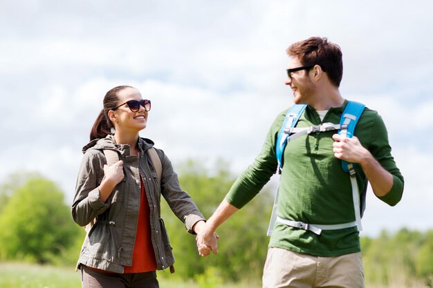 reizen, wandelen, backpacken, toerisme en mensen concept - gelukkige paar met rugzakken hand in hand en buiten wandelen