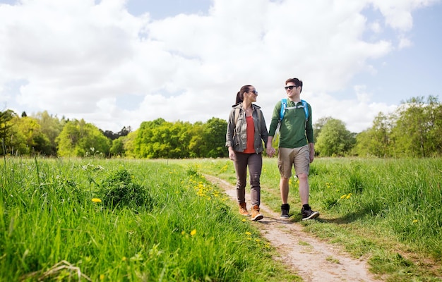 Foto reizen, wandelen, backpacken, toerisme en mensen concept - gelukkige paar met rugzakken hand in hand en wandelen langs landweg buitenshuis