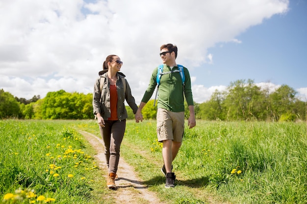 reizen, wandelen, backpacken, toerisme en mensen concept - gelukkige paar met rugzakken hand in hand en wandelen langs landweg buitenshuis