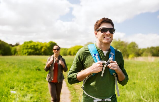 reizen, wandelen, backpacken, toerisme en mensenconcept - gelukkig stel met rugzakken die buiten langs de landweg lopen