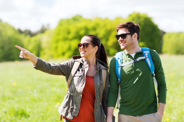 reizen, wandelen, backpacken, toerisme en mensenconcept - gelukkig stel met rugzakken die buiten lopen en met de vinger naar iets wijzen