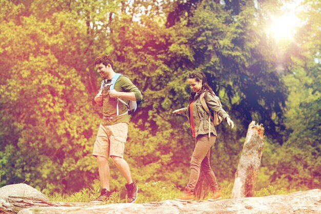 reizen, wandelen, backpacking, toerisme en mensen concept - gelukkig paar met rugzakken lopen langs gevallen boomstammen buiten