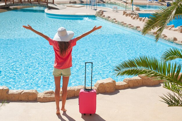 Reizen, zomervakantie en vakantieconcept. De mooie vrouw heft haar handen op dichtbij hotelpool.