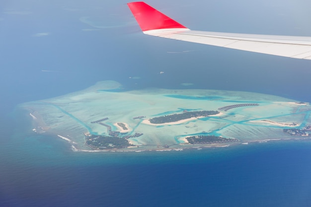 reizen, zomervakantie, transport, luchtvervoer en voertuigconcept - close-up van vliegtuigvleugel die boven het Maledivische eiland in de oceaan vliegt