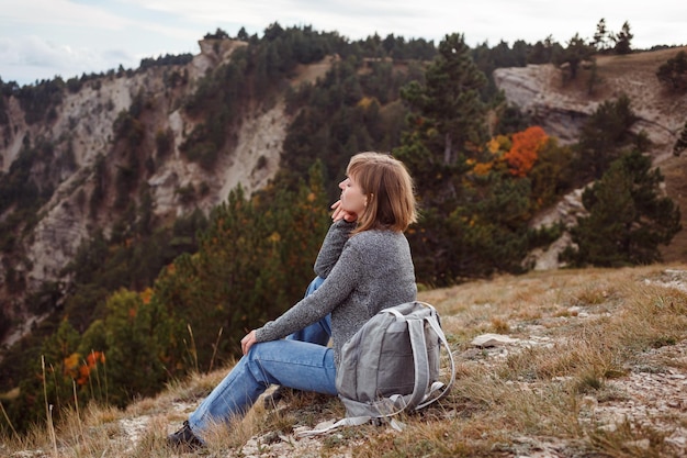 Reizende backpackervrouw zit op de berg voor prachtige beboste bergen