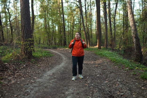 Reizende vrouw met rugzak die door een voorjaarsgroen bos loopt op een zonnige dag met een foto van hoge kwaliteit