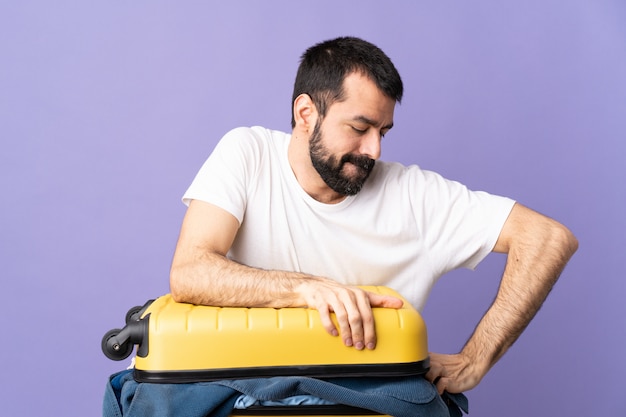 Reiziger blanke man met een koffer vol kleren over paarse muur