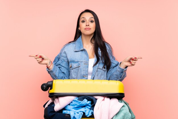 Reiziger Colombiaans meisje met een koffer vol roze kleren wijzend naar de zijkanten die twijfels hebben