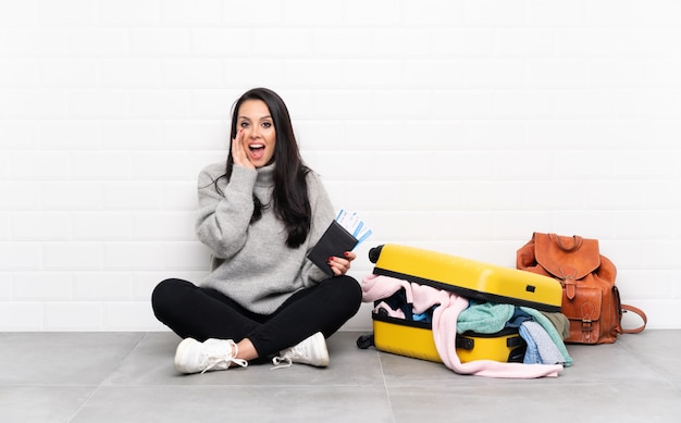 Reiziger Colombiaanse vrouw met een koffer vol kleren zittend op de vloer schreeuwend met wijd open mond