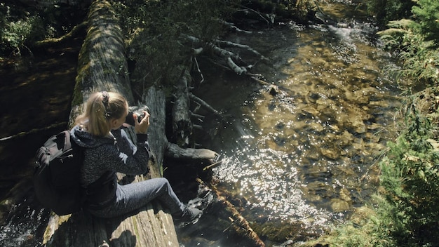 Reiziger fotograferen schilderachtig uitzicht in bos rivier Houten brug omgevallen boom Een blanke vrouw schieten mooie magische blik Meisje nemen foto video op camera Fotograaf reizen met rugzak Outdoor