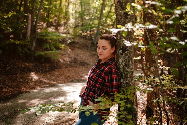 Reiziger hipster vrouw staan in herfst bos in geruit overhemd en spijkerbroek. Koud weer, herfstkleuren