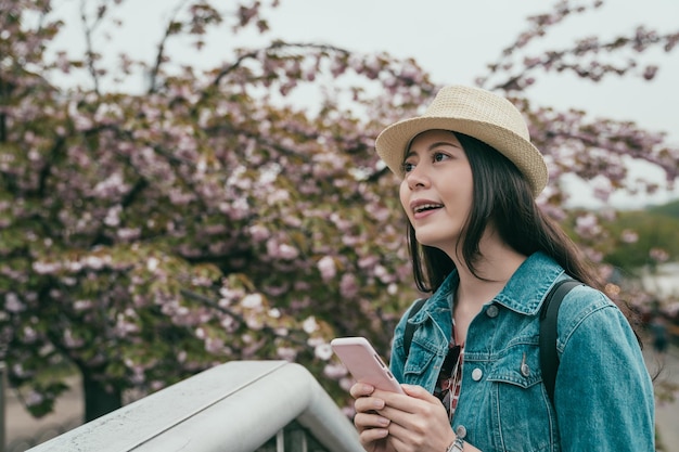 Reiziger houdt mobiele telefoon glimlachend vast en kijkt sakura