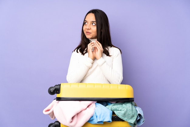 Reiziger jonge vrouw met een koffer vol kleren over geïsoleerde paarse iets gekonkel