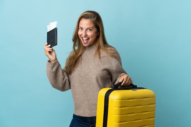 Reiziger middelbare leeftijd vrouw met een koffer geïsoleerd op blauw in vakantie met koffer en paspoort