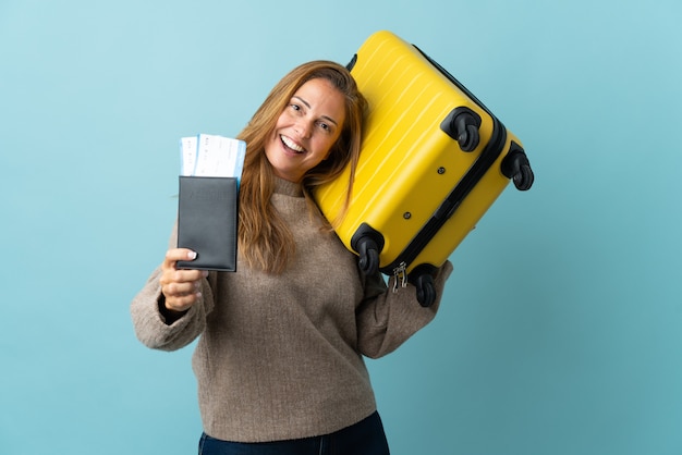 Reiziger middelbare leeftijd vrouw met een koffer geïsoleerd op blauwe muur in vakantie met koffer en paspoort