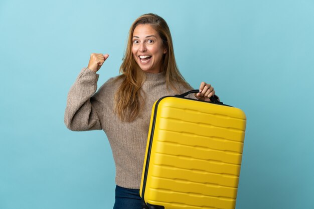 Reiziger middelbare leeftijd vrouw met een koffer geïsoleerd op blauwe muur in vakantie met reiskoffer