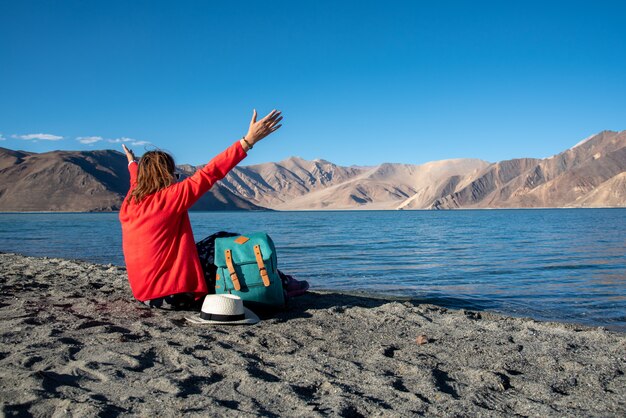 Reiziger rugzak vrouw opgeheven handen op het strand van Pangong Lake of Pangong Tso, Ladakh, Jammu en Kasjmir, India.