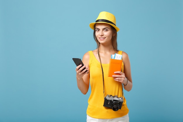 Reiziger toeristische vrouw in gele vrijetijdskleding hoed met kaartjes mobiele telefoon camera op blauw